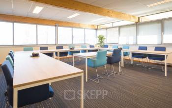 Spacious and well-lit office space rental at Steenovenweg 5 in Helmond, featuring large windows, blue chairs, and modern furniture.