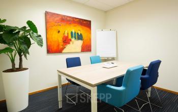 Interior of a furnished office space at Steenovenweg 5 in Helmond, featuring a conference table, chairs, a vibrant wall painting, and a large plant.
