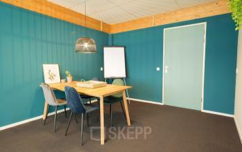 Office space at Steenovenweg 5, Helmond, featuring a meeting table with chairs, flipchart, and modern decor.
