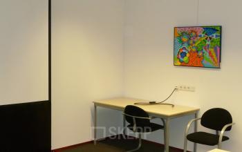 Modern office space rental at Jan Tinbergenstraat 202, Hengelo, featuring a vibrant painting, desk with chairs, and ample lighting.