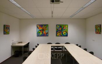 Office space rental at Jan Tinbergenstraat 202, Hengelo, featuring a conference room with a long table, bright artwork, and presentation equipment.