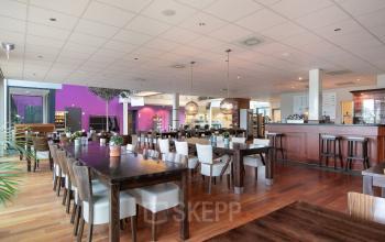 Spacious office interior at Jan Tinbergenstraat 202, Hengelo, featuring a well-lit workspace with wooden flooring, vibrant walls, modern furnishings, and seating ideal for collaborative work or office space rental.