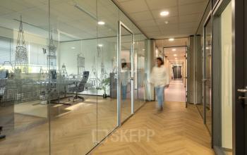 Modern office space at Hazenweg 2-2, Hengelo featuring glass-walled workspaces with a wooden floor and wall art.