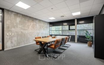 Modern conference room at Lintelerweg 40 in Hengelo featuring a large wooden table, leather chairs, and abundant natural light, perfect for office space rental.