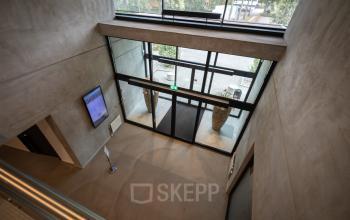 Entrance area inside the office building at Lintelerweg 40, Hengelo, with glass doors, modern decor, and a digital notice board.