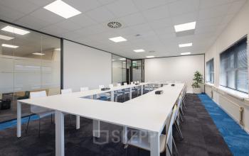 Modern office space rental at Lintelerweg 40 in Hengelo with large white tables, chairs, and glass partitions.