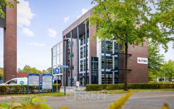 Exterior view of the office building located at Demmersweg 41-47 in Hengelo. The modern, multi-story structure is surrounded by trees and signage with the name 'VUMA' displayed on the facade.