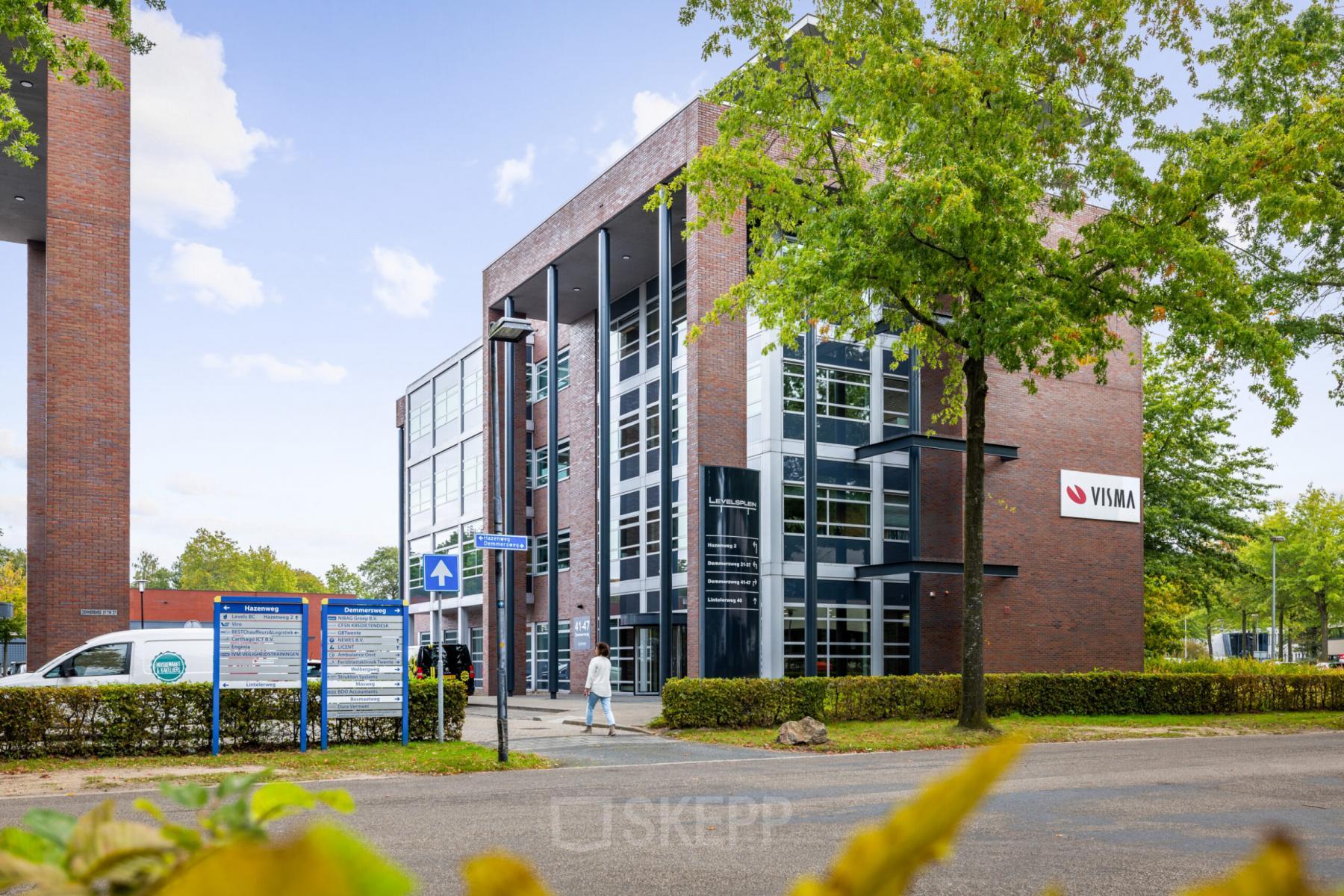 Exterior view of the office building located at Demmersweg 41-47 in Hengelo. The modern, multi-story structure is surrounded by trees and signage with the name 'VUMA' displayed on the facade.