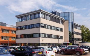 Exterior view of the office building at Welbergweg 60, Hengelo, available for rent office space. Multiple cars are parked outside the modern, multi-story building.