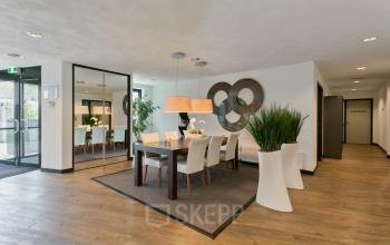 Contemporary office space at Welbergweg 60, featuring a polished meeting area with a wooden table, modern chairs, and vibrant greenery, available for rent.