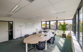 Bright office space for rent at Welbergweg 60, Hengelo, featuring a large oval table with chairs, whiteboard, and window views, ideal for meetings or collaborative work.