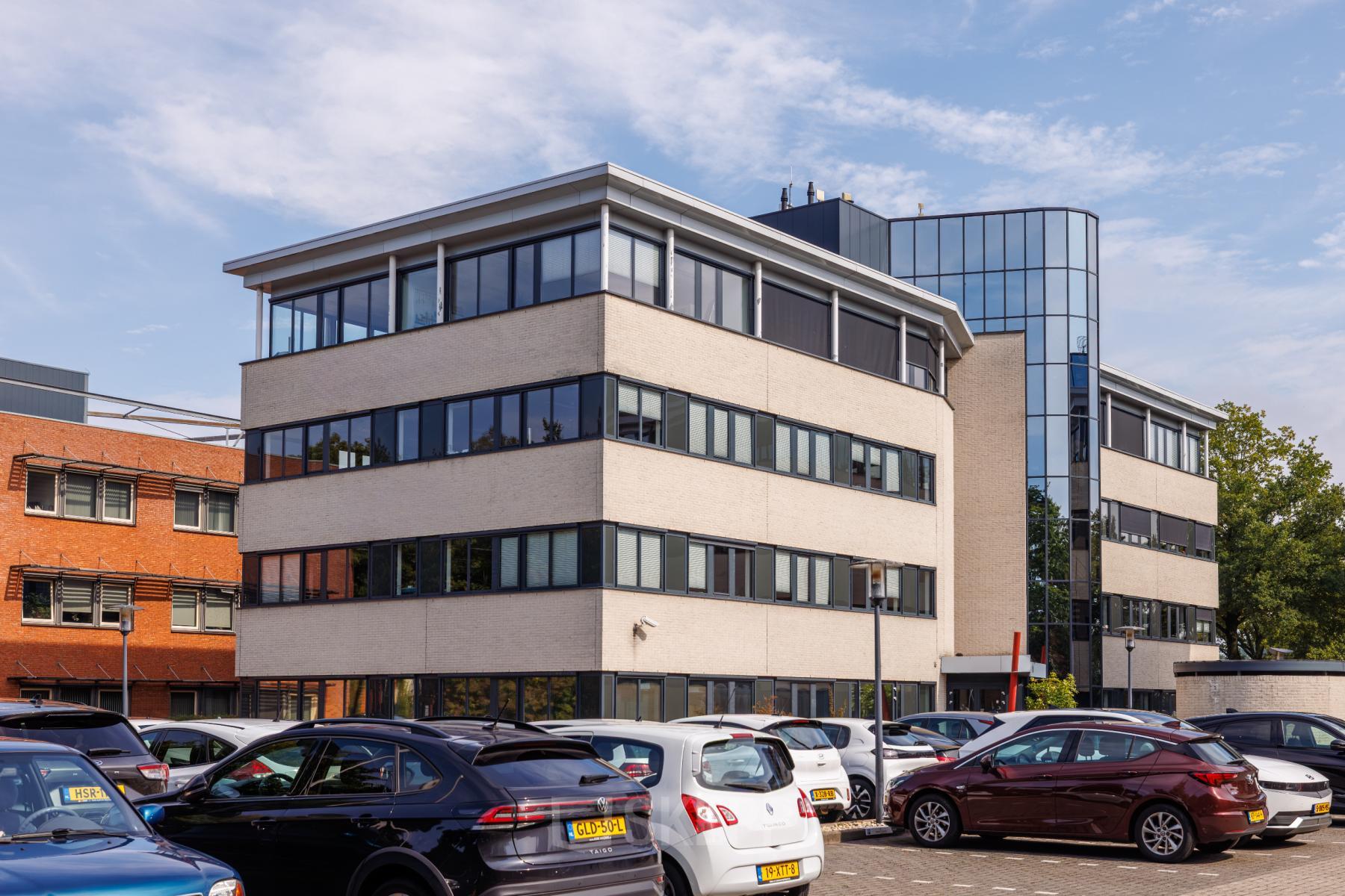 Exterior view of the office building at Welbergweg 60, Hengelo, available for rent office space. Multiple cars are parked outside the modern, multi-story building.