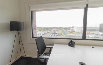 A small office space with a large window, an office chair, a white desk, a black desk lamp, and a parking lot view at Atealaan 34A, Herentals.