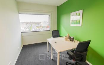 Bright office space rental at Atealaan 34A, Herentals, featuring green accent wall, window view, two desks, chairs, and phone.
