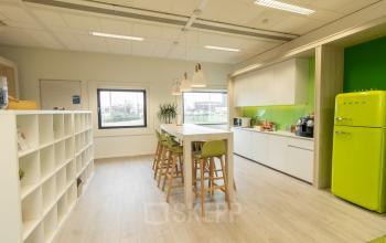 Modern furnished office kitchen space with green accents and a long high table, located at Atealaan 34A, Herentals. Ideal for office space rental.