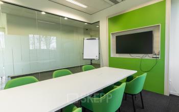 Modern meeting room with green accents at Atealaan 34A, Herentals, featuring a large table, chairs, a whiteboard, and a wall-mounted TV.