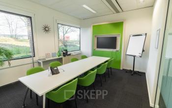 Modern conference room at Atealaan 34A, Herentals with green chairs, large table, TV, flipchart, and scenic windows.