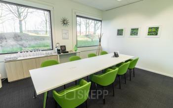 Modern conference room with a long white table and green chairs, large windows, and artwork on the wall at Atealaan 34A in Herentals.