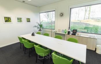 Light-filled conference room with green chairs, long white table, large windows, and minimalist decor at Atealaan 34A, Herentals, ideal for office space rental.