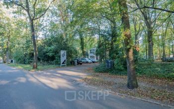 Exterior view of an office space available for rent at Mozartlaan 25, Hilversum, surrounded by trees and a parking area.
