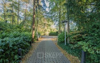 A serene pathway surrounded by lush greenery leads to the entrance of an office to rent at Mozartlaan 25, Hilversum.
