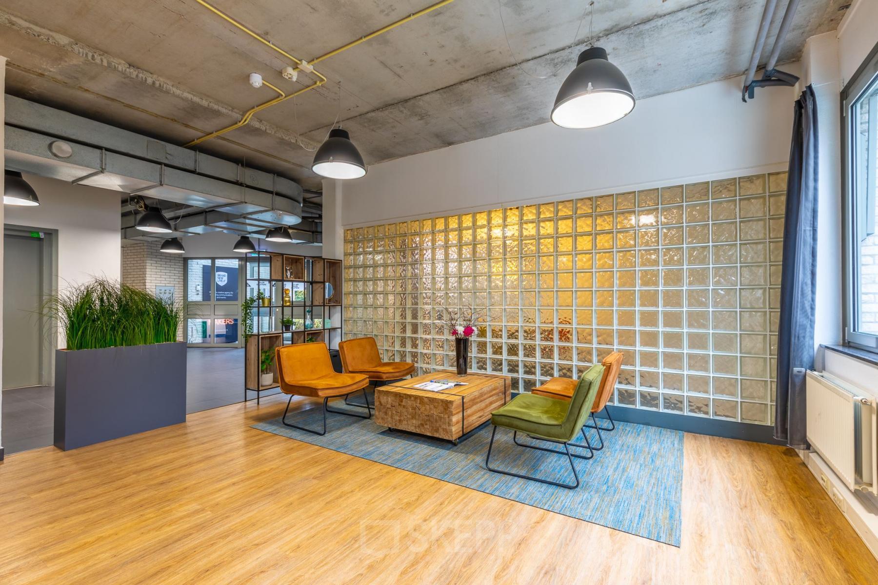 Modern office space at Mozartlaan 25, Hilversum with stylish seating area featuring armchairs, a wooden table, and a decorative glass block wall.