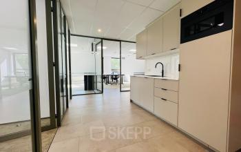 Modern office space available for rent in Hilversum's Marathon 2, featuring a sleek kitchenette beside spacious workspaces.