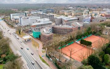 Aerial view of the Olympia 4 office complex in Hilversum, featuring modern architecture surrounded by greenery and adjacent tennis courts. Ideal location for office space rental with easy access to main roads.