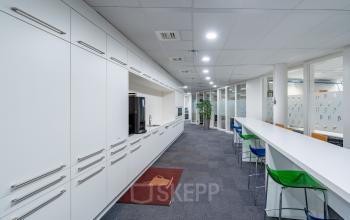Modern office space in Hilversum featuring a long corridor with cabinets, a spacious countertop with colorful stools, and glass partition walls, ideal for office space rental.