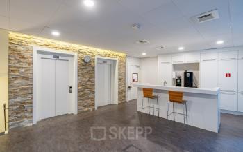 A modern pantry area in an office at Olympia 4, Hilversum, featuring a stylish kitchenette with white cabinetry and bar stools, perfect for office space rental.