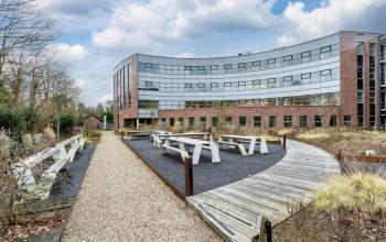 Modern office exterior at Olympia 4, Hilversum with a curved facade and outdoor seating area, ideal for breaks. Prime location for office space rental in a professional environment.