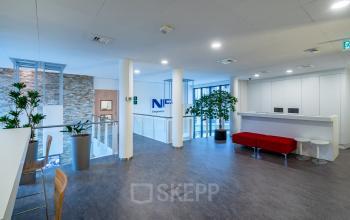 Modern office interior at Olympia 4, Hilversum featuring a spacious layout with a sleek seating area, bar-height tables, and lush plants, ideal for office space rental.