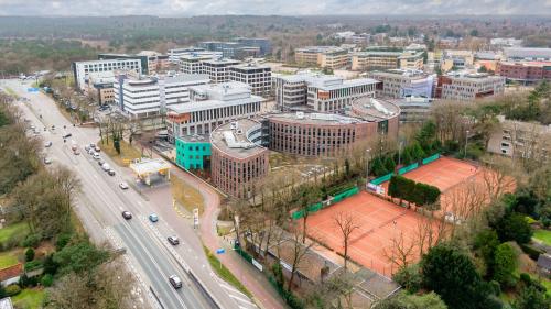 Aerial view of the Olympia 4 office complex in Hilversum, featuring modern architecture surrounded by greenery and adjacent tennis courts. Ideal location for office space rental with easy access to main roads.