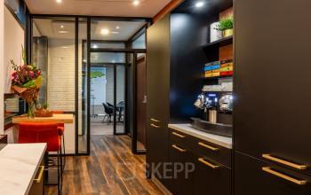 Furnished office space for rent at Steijnlaan 16, Hilversum, featuring sleek cabinetry and a coffee station, leading to a meeting area.