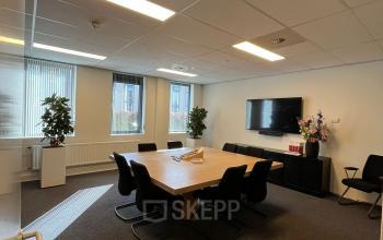 Modern office space in Hilversum with a large wooden table, surrounded by black chairs, suitable for meetings. Bright lighting and indoor plants add a fresh touch. Ideal for office space rental.