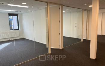 Unfurnished office space at Catharina van Renneslaan 8-10, Hilversum, featuring glass partitions and carpeted floors, ideal for office to rent solutions.