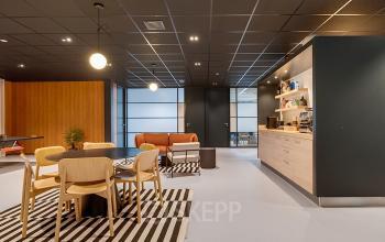 Modern office space in Hoevelaken featuring a comfortable seating area with wooden chairs, a lounge, and a kitchenette. Ideal for those seeking office space rental with a stylish interior.