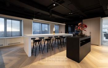 Modern workspace with minimalist design, wooden flooring, high tables, and stools at Polarisavenue 1, in Hoofddorp, ideal for office space rental.