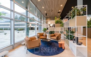 Modern office to rent at Polarisavenue 1, Hoofddorp featuring a stylish lounge area with comfortable seating, a blue rug, and large windows letting in natural light.