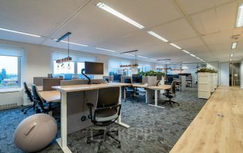 Modern office space available for rent at Polarisavenue 1, Hoofddorp, featuring large workstations, ergonomic chairs, and abundant natural light with views through wide windows.
