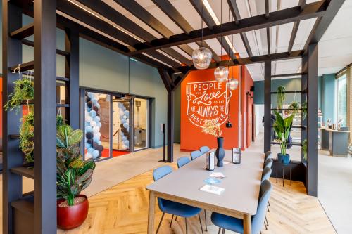 A modern furnished workspace at Spicalaan 1-59, Hoofddorp, featuring a long table with blue chairs, greenery, and decorative lights, ideal for office space rental.