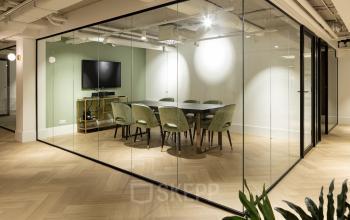 Modern conference room at Siriusdreef 60, Hoofddorp, featuring a large round table, green chairs, and a wall-mounted TV. Ideal office space rental for productive meetings.