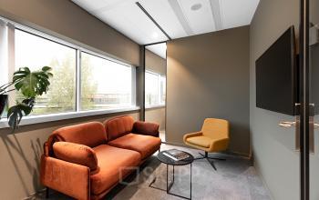Cozy furnished office space at Taurusavenue 1-41, Hoofddorp, featuring an orange sofa, a yellow chair, a table, and a wall-mounted screen for an ideal office space rental.
