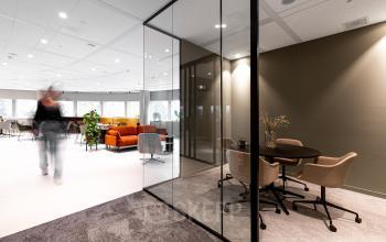 This modern office space at Taurusavenue 1-41 in Hoofddorp features stylish glass partitions, cozy seating, and a person walking through, ideal for businesses looking for office space rental.