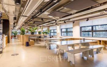 Spacious and modern office interior at Siriusdreef 16, Hoofddorp, featuring furnished workspaces with tables, benches, and greenery. Ideal office space rental opportunity.