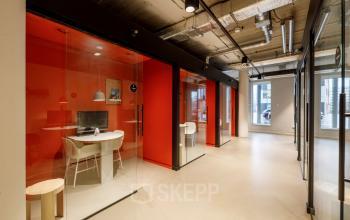 Modern office space rental at Siriusdreef 16, Hoofddorp, featuring a corridor with vibrant red glass enclosed meeting rooms and stylish lighting.