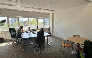 Bright office space at Planetenweg 5, Hoofddorp, featuring large windows and multiple workstations. A person is working at a desk, showcasing an ideal spot for office space rental.