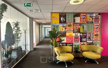 Bright hallway at Planetenweg 5 in Hoofddorp with vibrant posters on the walls, stylish chairs, and lush plants, offering a welcoming space for office activities.
