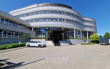 Exterior view of the office building at Planetenweg 5, Hoofddorp, showcasing modern architecture with a curved facade, large windows, and entrance steps. Ideal for businesses seeking office space rental in a strategic location.