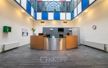 Spacious reception area with modern furnishings at Siriusdreef 17 offering office space rental in Hoofddorp, with a professional at the desk.